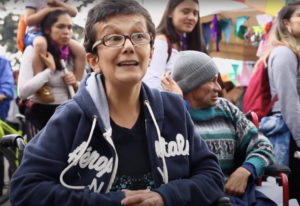 Yolanda Gil, integrante de Polimorfas, mujer de tez morena, lleva unas gafas color café, un buzo deportivo azul oscuro y una camiseta negra. Está sentada en una silla de ruedas en medio de la multitud de una marcha.