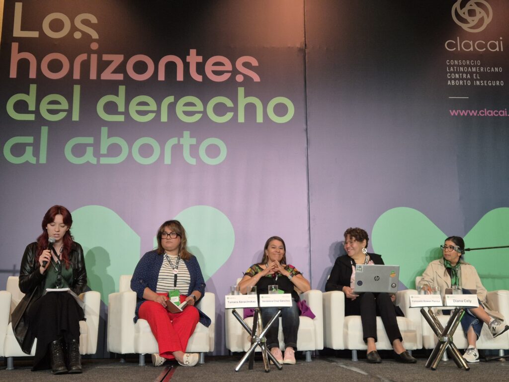 La iamgen muestra a 5 mujeres sentadas en sillones blancos una junto a otra en el marco del evento "Los horizontes del derecho al aborto"